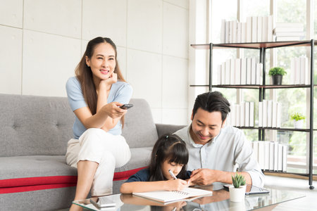 Portrait of happy daughter sitting and doing her homework relaxing with her family at home.の写真素材