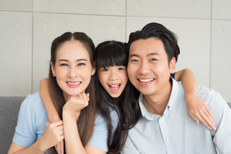 Portrait of happy mother father and daughter family sitting on couch together relaxing at home.の写真素材