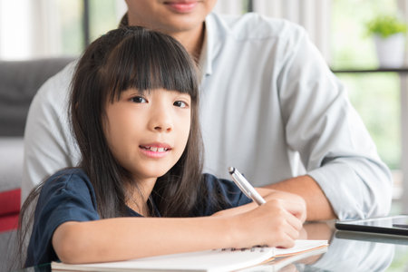 Portrait of happy daughter sitting and doing her homework relaxing with her family at home.の写真素材