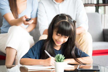 Portrait of happy daughter sitting and doing her homework relaxing with her family at home.の写真素材