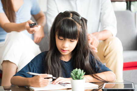 Portrait of happy daughter sitting and doing her homework relaxing with her family at home.の写真素材