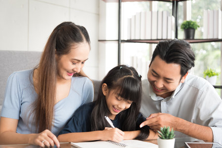 Happy daughter sitting and doing her homework relaxing with her father and mother family at home.の写真素材