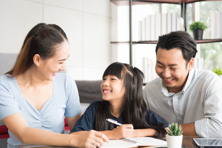 Happy daughter sitting and doing her homework relaxing with her father and mother family at home.の写真素材