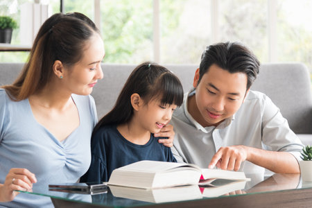 Happy family sitting together and help teaching daughter about her homework in living room.の写真素材
