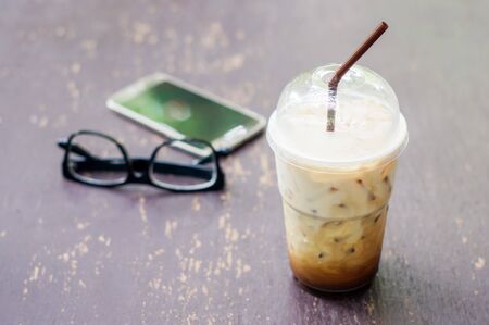 Iced coffee, smartphone and glasses on the wood table.の写真素材