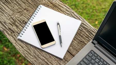 Laptop, smartphone, pen, and book on a wooden table.の写真素材