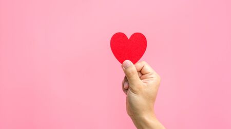 Hand holding a red fabric heart in a pink background.の写真素材