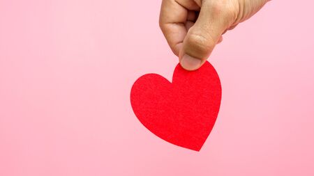 Hand holding a red fabric heart in a pink background.の写真素材