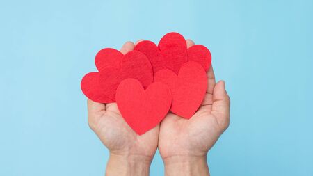 Hand holding a red fabric heart on a blue background.の写真素材