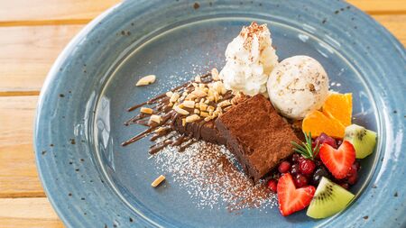 Chocolate brownie cake with ice cream and mix fruit on a blue plate.の写真素材