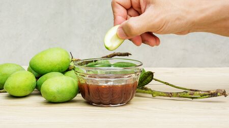 Green sour mango (raw mango) with sweet fish sauce on a wooden table.の写真素材