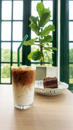 Iced latte coffee and chocolate cake on a wooden table in a cafe.の写真素材