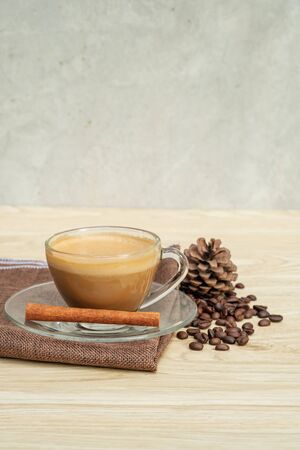 A cup of hot coffee and cinnamon on a wooden table.の写真素材