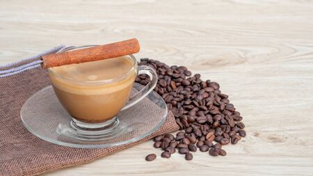 A cup of hot coffee and cinnamon on a wooden table.の写真素材