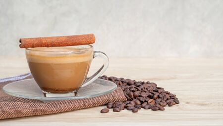 A cup of hot coffee and cinnamon on a wooden table.の写真素材