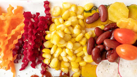 Corn, beetroot, carrot, red bean, and tomato on a white plate.の写真素材