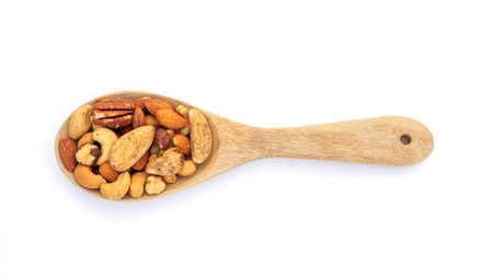 Baked mixed nuts in a wooden spoon on a white background.の写真素材