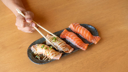chopsticks tong fresh salmon sushi on a wooden table.の写真素材