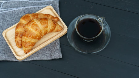 Croissant and black coffee on a black wooden table.の写真素材