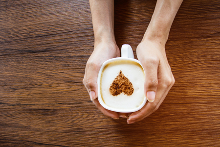 hand of woman with heart on latte art coffee on wooden table with vintage tone. Soft focusの写真素材