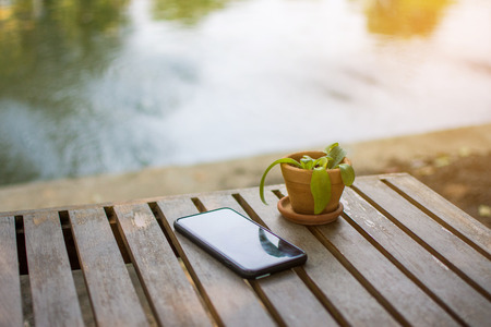 black smart phone on wooden table and plant. subject is blurred.