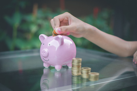 children's hand put money coin on pink pig piggy bank and nature background. soft focus.の写真素材