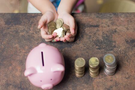 cute little girl holding coin of money and put in pink piggy bank with blur background. subject is...