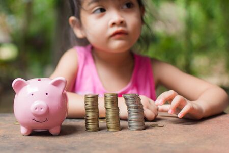 cute little girl holding coin of money and put in pink piggy bank with blur background. subject is blurred.の写真素材