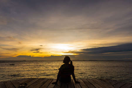 silhouette of woman jumping on the sea at sunset. soft focus and low keyの写真素材