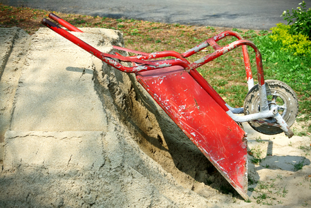 Red One-Wheel Construction Cart Parking on a Pile of Sand Near Construction Siteの写真素材