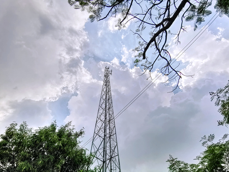Low Angle View of Telecommunication Tower Through Tree Canopy Against Cloudy Skyの写真素材