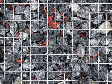 Full Frame Background of Gravel Stones with Dry Leaves Under Metal Wire Meshの写真素材
