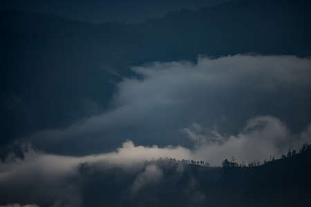 beautiful landscape of hills silhouette during sunrise. light breaking through cloud cover. mist covered mountains and hillsの写真素材
