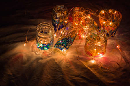 beautiful colorful hand painted glass bottles and cups illuminated with miniature christmas lights during festival celebration. copy space background. dark background night shot. selective focus.の写真素材