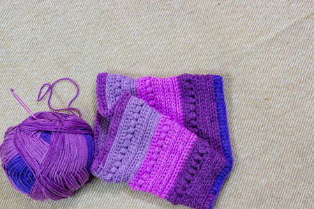 colorful ball of wool and piece of woven winter garment with crochet needle or hook against light...