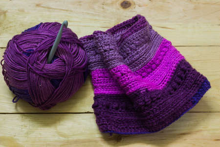 colorful ball of wool and piece of woven winter garment with crochet needle or hook against light...