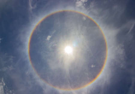 circular rainbow halo around the sun among blue sky and white clouds. natural phenomenon due to light interacting with suspended particles.の写真素材