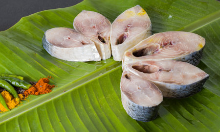 Raw hilsa fish cut into pieces kept on banana leaf for cooking. Shot taken in studio with copy space background and spices.の写真素材