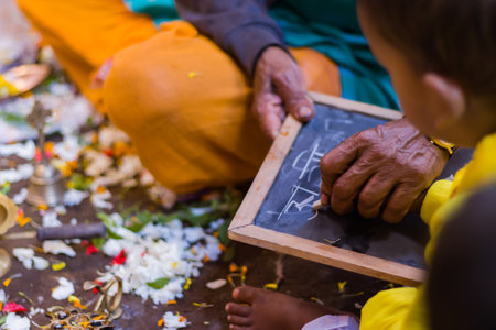 Priest is teaching young child to write Hindi letters with chalk and slate during aksharabhyasam or hate khori ritual during Saraswati Puja or vasant panchami festival in indiaの写真素材