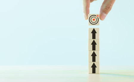Business achievement goal and objective target concept. Hand placing final wooden block with a target symbol, symbolizing goal achievement and strategic planning. Copy space, business growth,の写真素材
