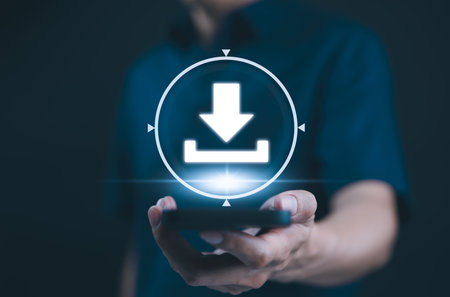 Download Technology for Data Storage and Transfer. A person holds smartphone with glowing download icon, symbolizing digital data storage, cloud services, technology for transferring files and media.の写真素材
