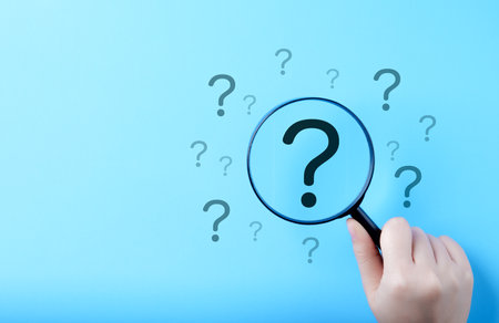 Question Mark and Root Cause Analysis Concept. A hand holding a magnifying glass over a large...