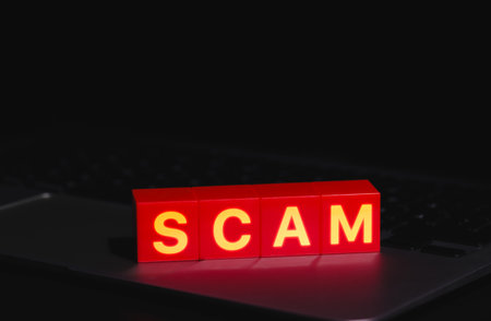 Red Scam Blocks Highlighting Cyber Fraud. Spelling SCAM placed on laptop keyboard in dark environment, symbolizing cyber fraud, phishing, scammer, cybersecurity threats, and online deception risks.の写真素材