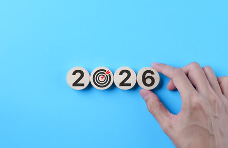 2026 goal setting concept. Hand arranging wooden blocks and target icon on blue background, symbolizing business planning, vision execution, future strategy and performance objectives. 2026 new year,の写真素材