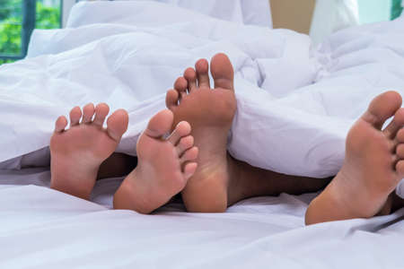 Feet of couple side by side in bedの写真素材