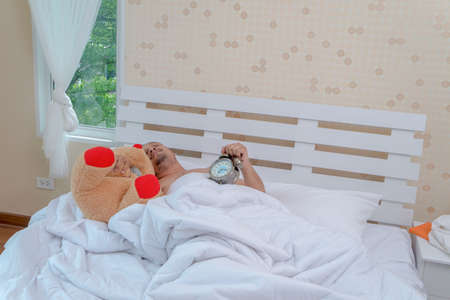 Men are awake with a front alarm clock on a white bed.の写真素材
