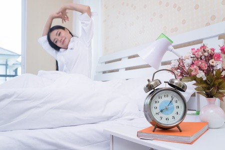 Closeup alarm clock has a nice day with a happy woman in bed after waking up after waking up.の写真素材