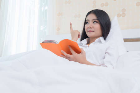 Woman lying in bed while reading a bookの写真素材