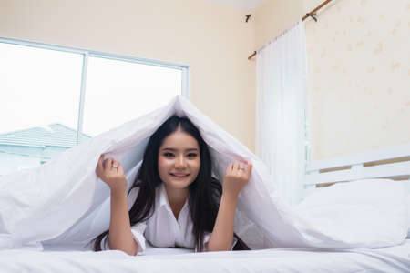 hiding under blanket. Woman smiling and looking aside.の写真素材