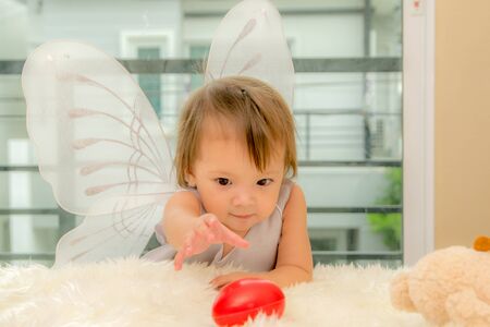 1 year old girl Year standing at the edge of the bed trying to catch toys on the couch.の写真素材